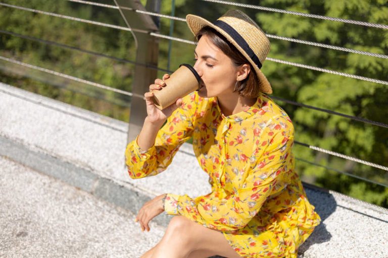 kobieta w kapeluszu i żółtej sukience pije kawę
